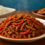 Plato de ropa vieja cubana con pimientos y cebolla, acompañado de arroz blanco y plátanos maduros fritos.
