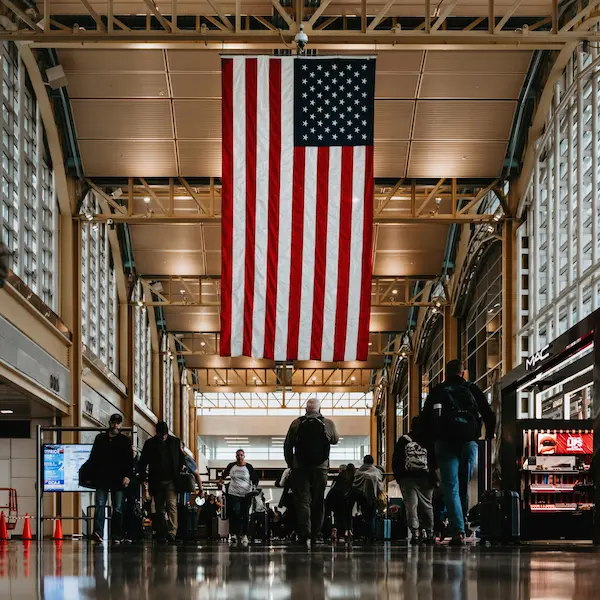 Personas en un aeropuerto con bandera de Estados Unidos como símbolo de emigrar y empezar de nuevo